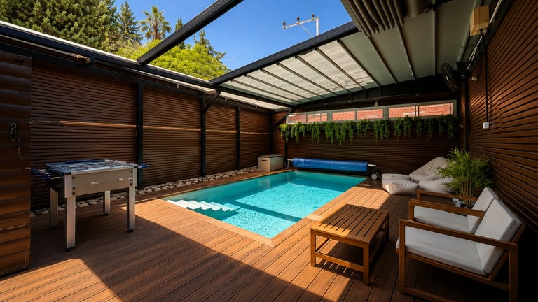 Modern backyard patio with retractable roof, swimming pool, wooden deck, lounge chairs, and foosball table surrounded by privacy screens